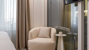 A modern hotel room with a plush armchair, a small table with a cup, and a large window with curtains. - Elegance Room in Split (Split)