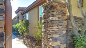 A residential building with a stone facade, a visible window, and a small garden area with plants and a tree. - Cathedral City Home w/ Private Pool - Near Golf (Cathedral City)