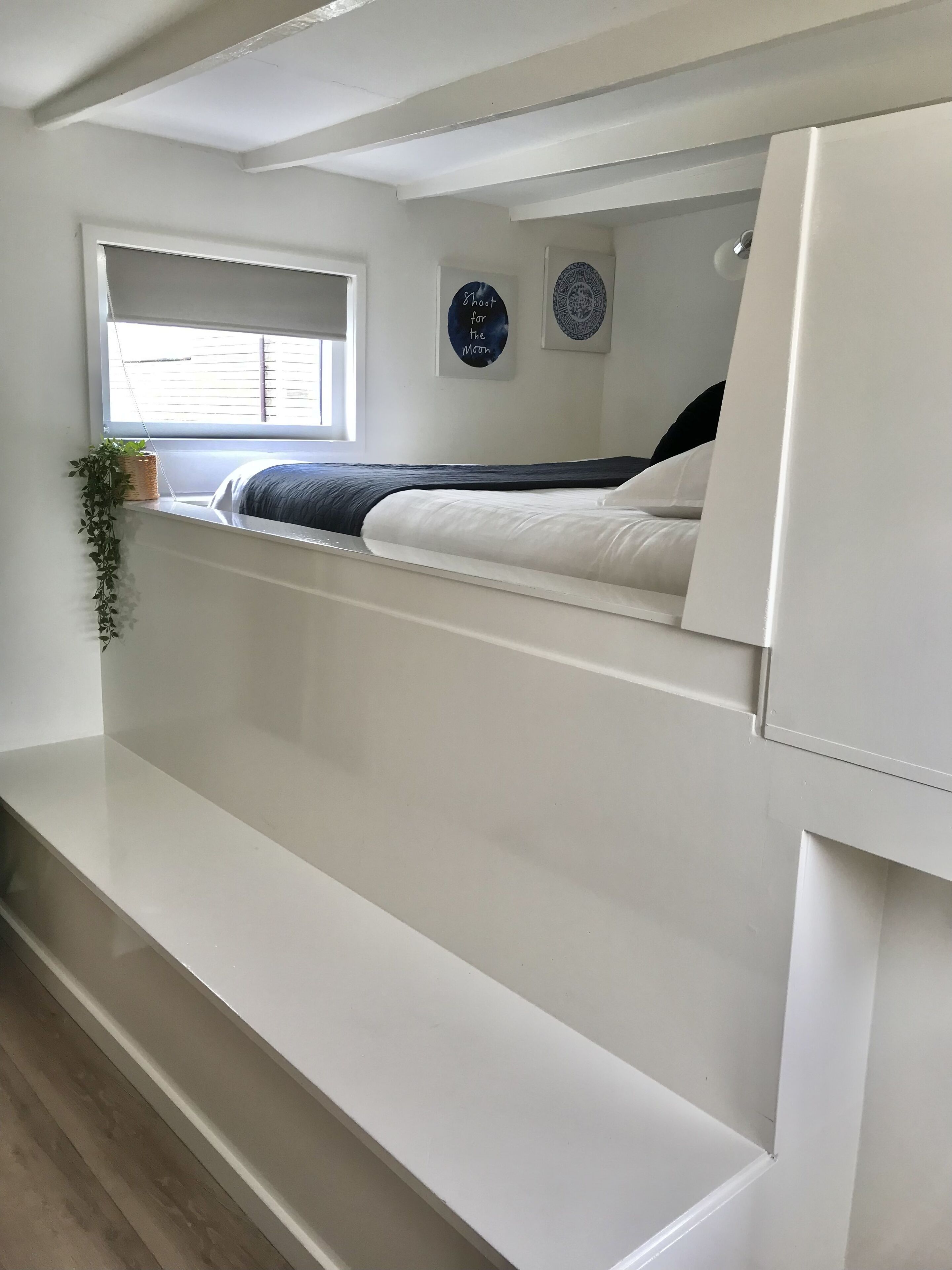 Une chambre à coucher comprenant un lit, une fenêtre, une étagère fixée au mur avec une plante, et deux éléments de décoration murale.
