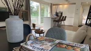 Una sala de estar moderna con un sofá, una mesa de centro con revistas, y un jarrón grande con ramas.