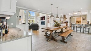 Una cocina amplia con isla central, iluminación colgante y una zona de comedor con sillas.
