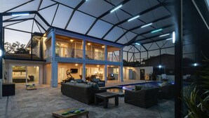Un amplio espacio al aire libre con piscina, un porche cubierto y un edificio de dos pisos con varias habitaciones.