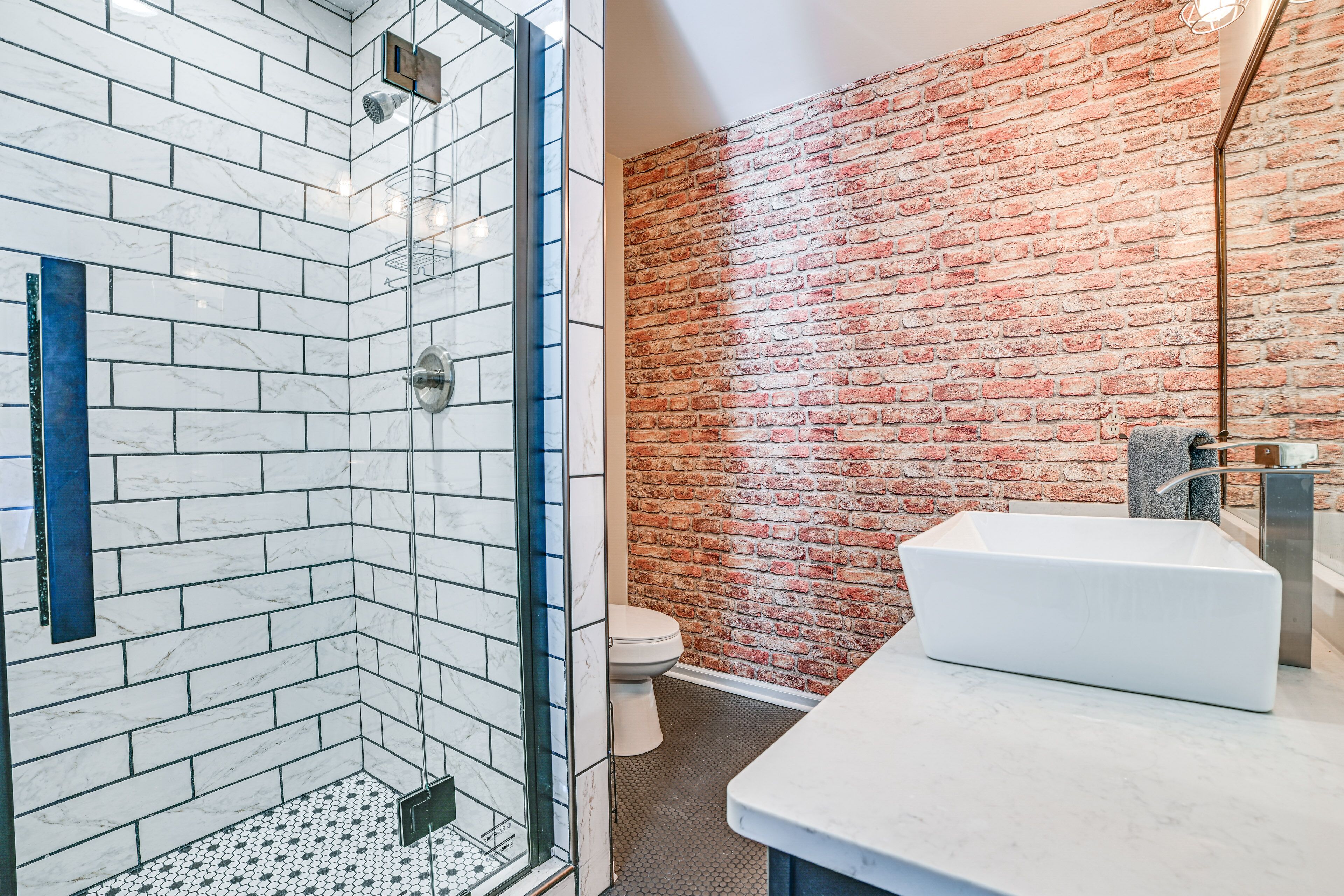 Ein modernes Badezimmer mit einer gläsernen Duschkabine, einem weißen Waschbecken und einer Ziegelwand.