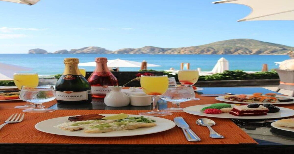 A table set with food and drinks, overlooking a coastal landscape.