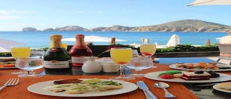 A table set with food and drinks, overlooking a coastal landscape.