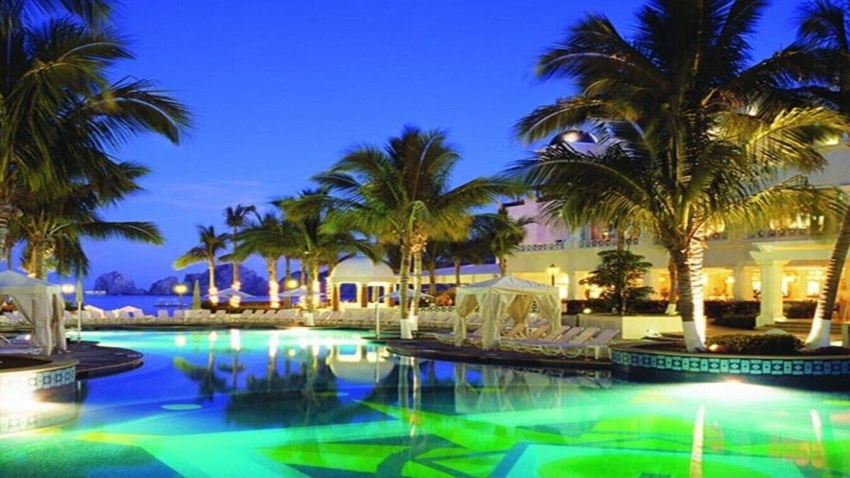 A pool area with palm trees, lounge chairs, and a night-time setting.