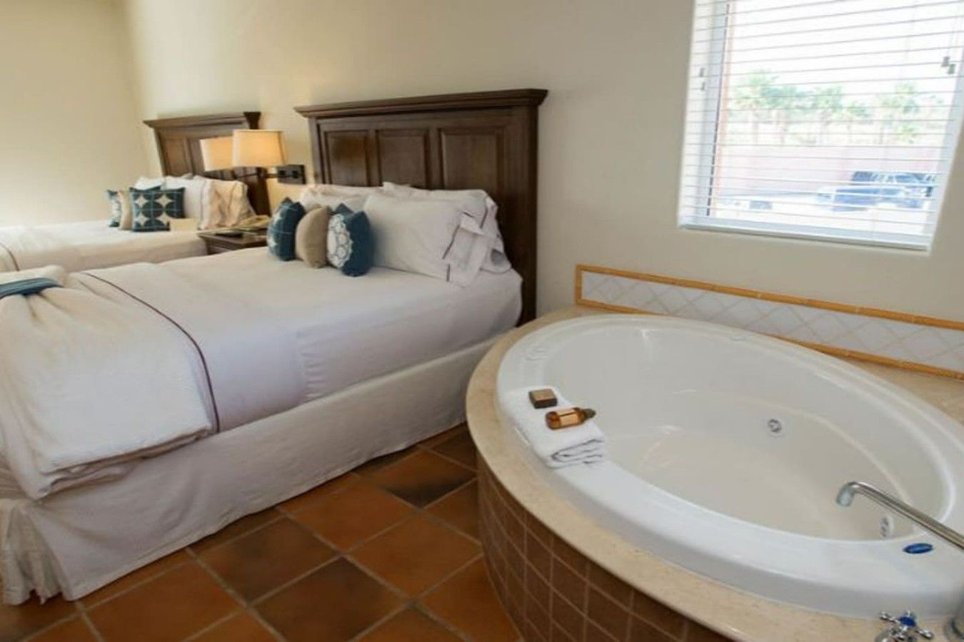 A bedroom with two beds, a large bathtub, and a window with blinds.