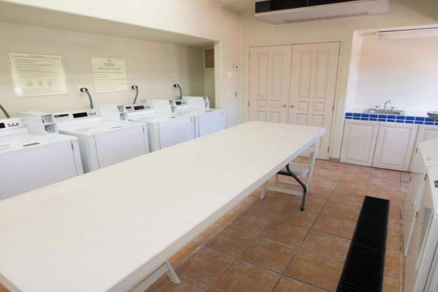 A laundry room with multiple washing machines, a long table, and a tiled floor.