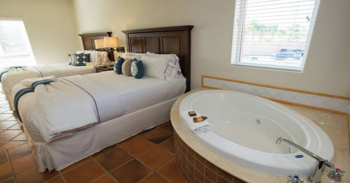 A hotel room with a large bed, a separate sitting area, a bathtub, and a window with blinds.