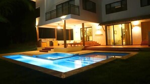 Ett modernt hus med en swimmingpool, en täckt uteplats och en trappa som leder upp till ett andra våningsplan.