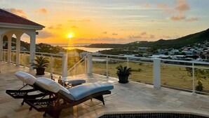 A terrace with lounge chairs and a view of a sunset over a town.