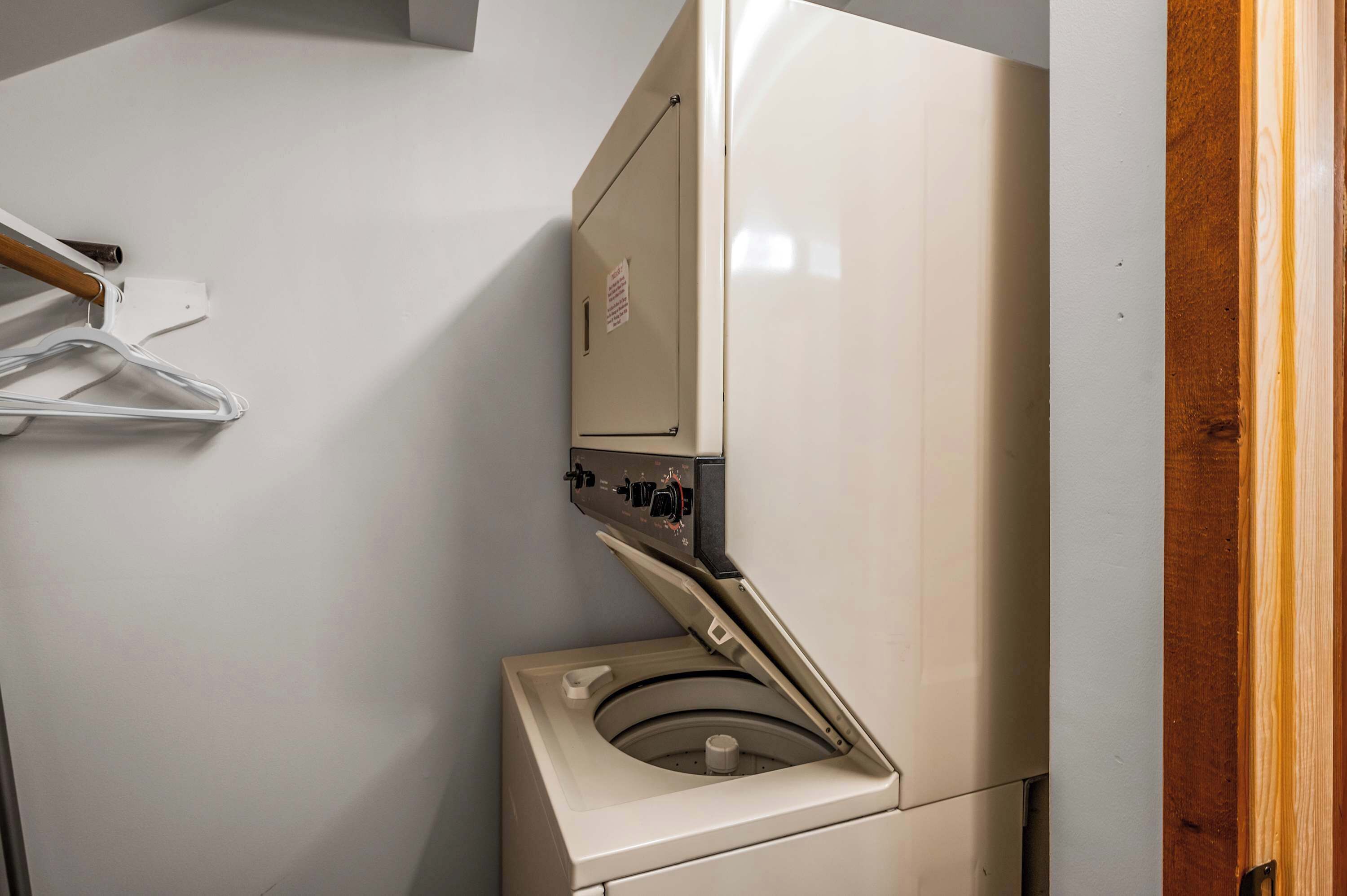 Una lavadora blanca y compacta con panel de control, una puerta de madera y un tendedero fijado a la pared.