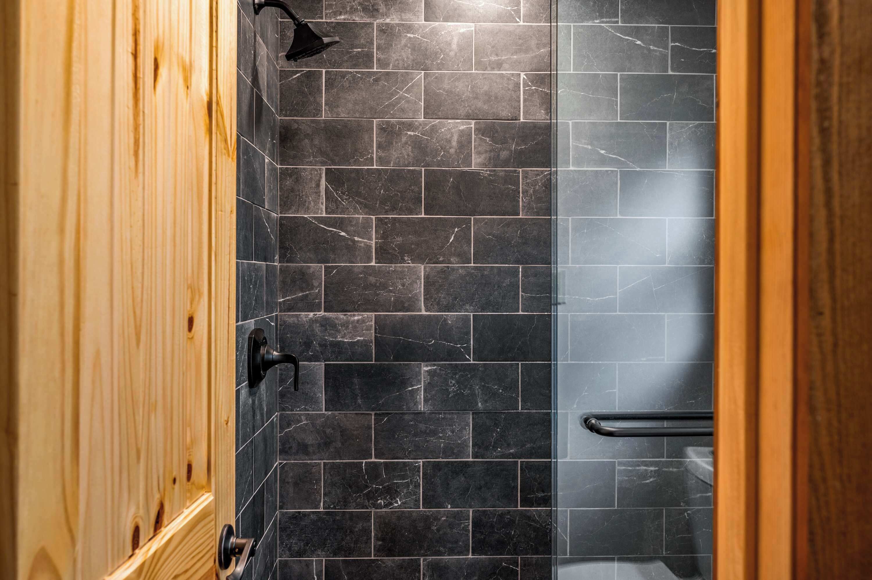 A bathroom with dark marble tiles, a wooden door, and a glass shower enclosure.