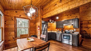 A wooden cabin interior with a dining table, chairs, a refrigerator, a stove, and cabinets.