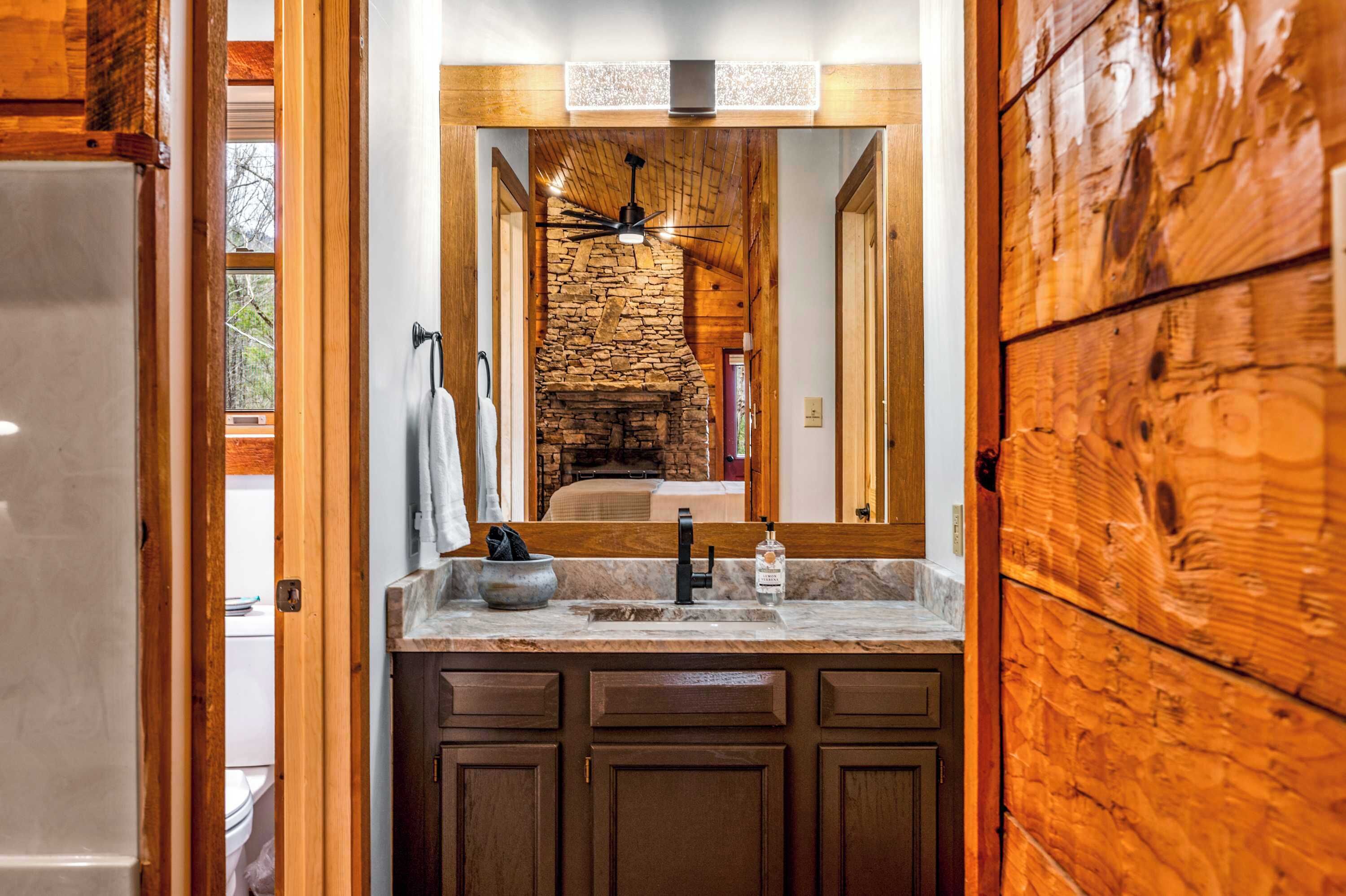 A bathroom with a stone fireplace, wooden cabinets, and a large mirror.