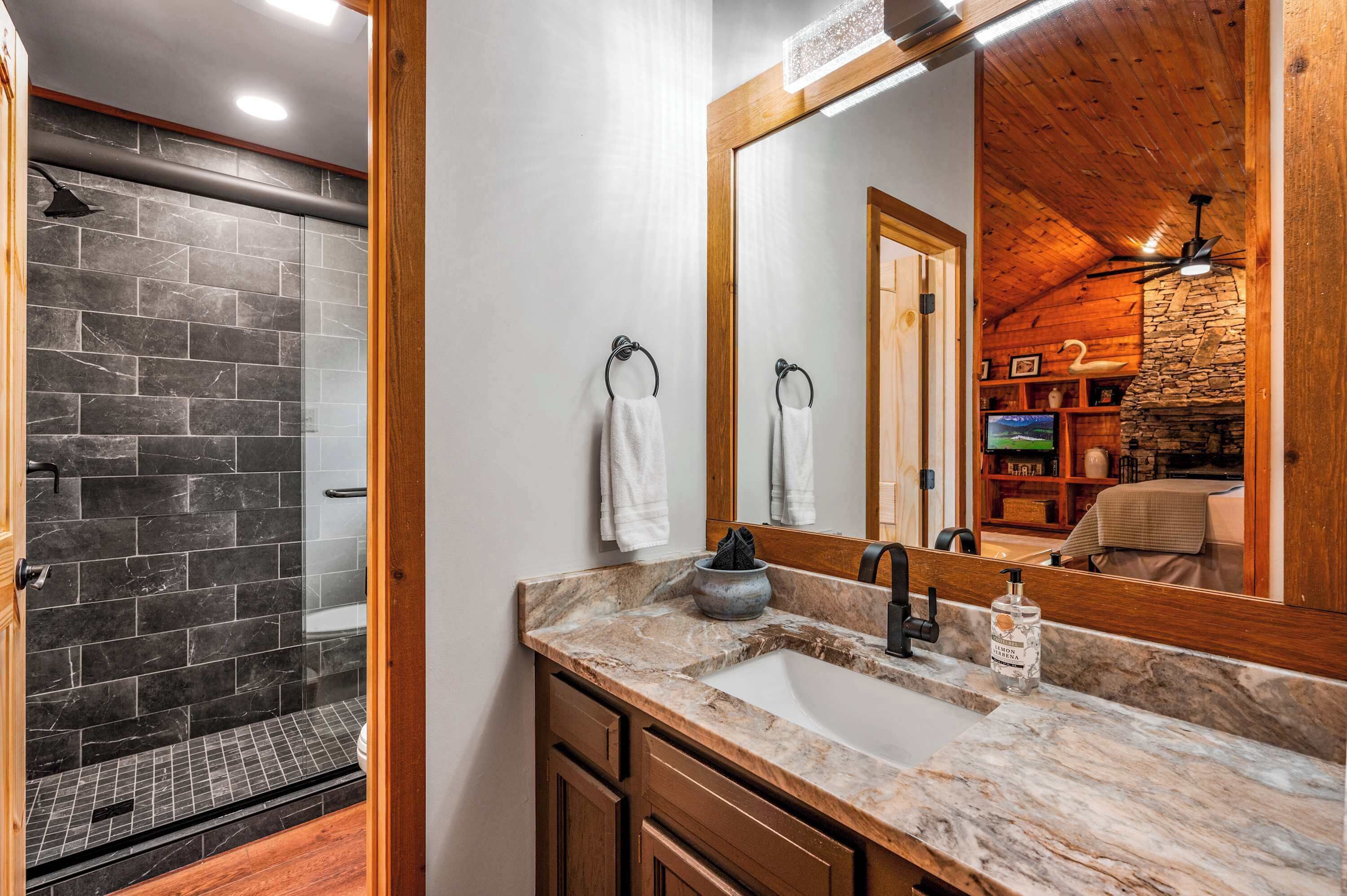 A bathroom with a stone shower, a sink with a marble countertop, and a large mirror reflecting the room.