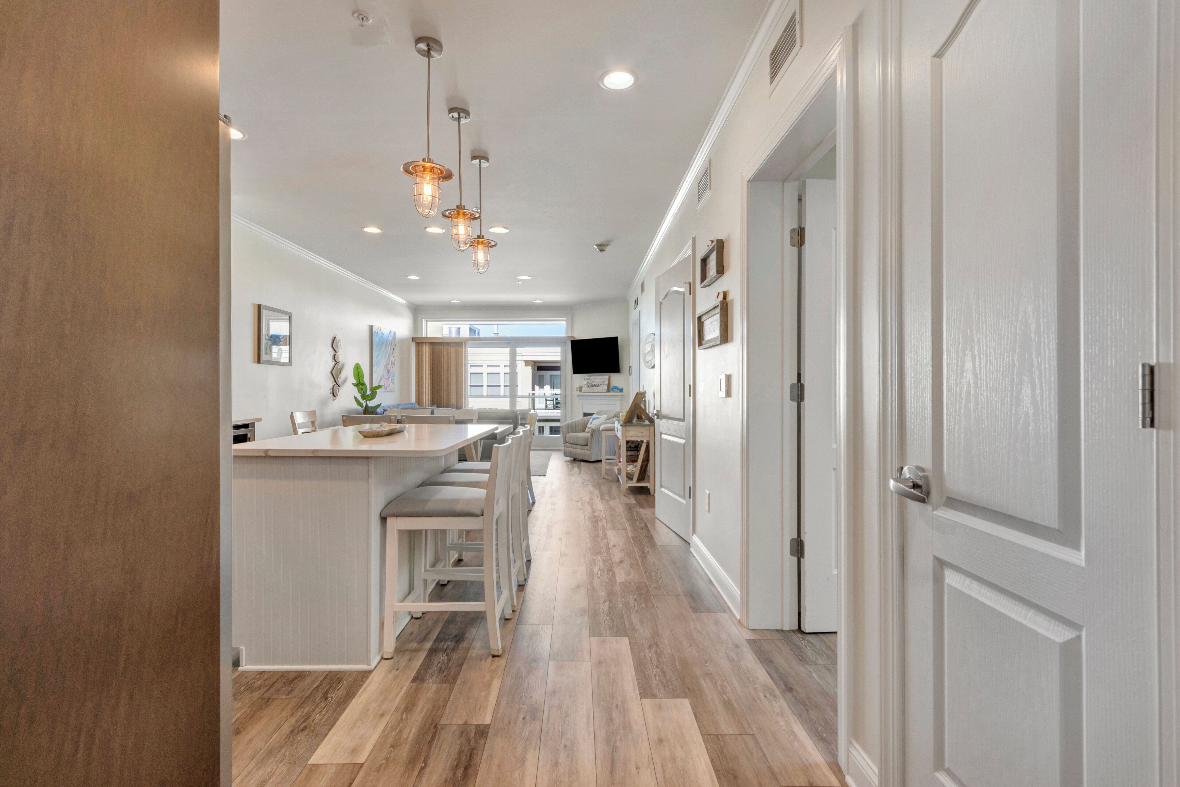 A modern kitchen with a central island, pendant lighting, and a view into the dining area.