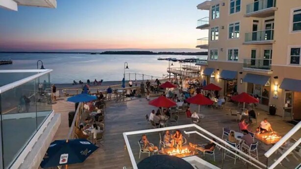 A deck area with outdoor seating and a fire pit, overlooking a body of water. - Fabulous Beach Retreat overlooking the Pool  (Dewey Beach)