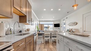 A modern kitchen with wooden cabinets, a large island, and a dining area with chairs. - Fabulous Beach Retreat overlooking the Pool  (Dewey Beach)