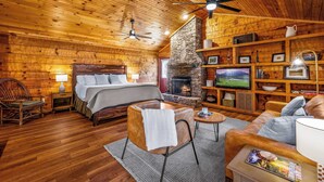 A cozy log cabin interior with a bed, seating area, fireplace, TV, and wooden walls. - Mountain-Modern Cabin w/BIG Jet Tub (Townsend)