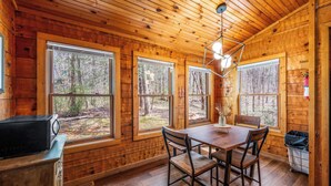 A wooden cabin interior with a dining table, chairs, a microwave, and large windows. - Mountain-Modern Cabin w/BIG Jet Tub (Townsend)