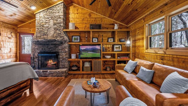 A cozy cabin interior with a stone fireplace, wooden walls, a leather sofa, and a television. - Mountain-Modern Cabin w/BIG Jet Tub (Townsend)