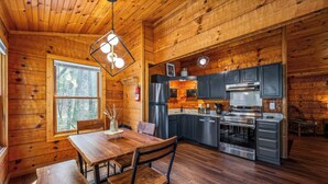 A wooden cabin interior with a dining area, kitchen, and large window. - Mountain-Modern Cabin w/BIG Jet Tub (Townsend)