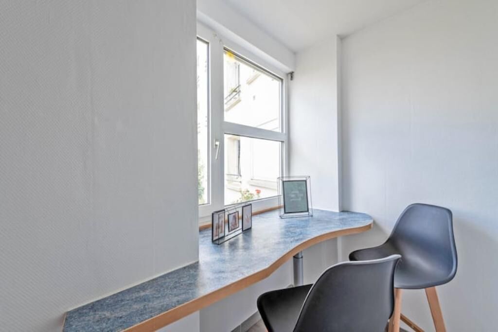 A modern room with a curved desk, two black chairs, and a window with a view of buildings.