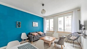 Uma sala de estar moderna com parede azul, um sofá cinza, uma mesa de jantar branca e uma cadeira preta.