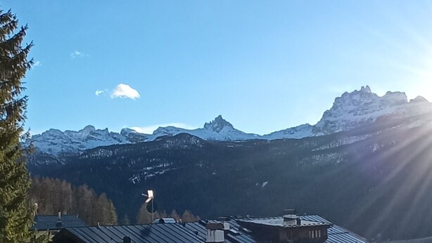 A mountain village with traditional wooden houses, a wooden bridge, and a view of snow-capped mountains under a clear sky. - Breathtaking Panorama  (Cortina d'Ampezzo)