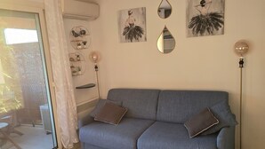 A living room with a grey sofa, two cushions, a floor lamp, and wall art. - Appartement Côte D'azur Accès Direct Plage (Théoule-sur-Mer)