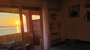 A room with a bed, a chair, a table, and a view of the sunset over the sea. - Appartement Côte D'azur Accès Direct Plage (Théoule-sur-Mer)