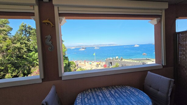 A room with a view of the sea, a small round table, and a window with blinds. - Appartement Côte D'azur Accès Direct Plage (Théoule-sur-Mer)