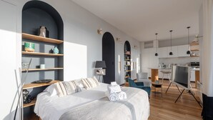 Moderni hotellihuone, jossa on suuri sänky, puuhyllyt, työpöytä ja televisio.