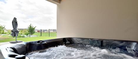 A hot tub with water, a wooden ceiling, and a view of a grassy area and a fence.