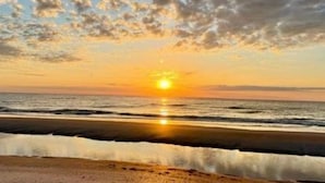 Una playa con el sol poniéndose sobre el océano, reflejado en el agua.
