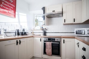 Una cocina moderna con armarios blancos, horno integrado, microondas y cafetera.