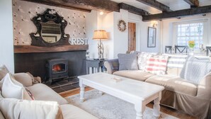 A cozy living room with a fireplace, a sofa set, a white coffee table, and a wall-mounted mirror. - Milan Cottage - 2 Bedroom Cottage - Port Eynon (Swansea)