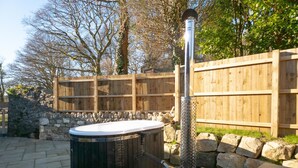 A hot tub with a stone wall and wooden fence in the background. - Suite 14 - Sleeping Giant Hotel - Pen Y Cae Inn (Swansea Valley)