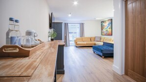A modern living room with a sofa and a blue ottoman, a wooden dining table with a tray, and a potted plant. - Suite 14 - Sleeping Giant Hotel - Pen Y Cae Inn (Swansea Valley)