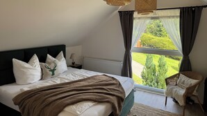 A bedroom with a bed, a chair, and a window with a view of greenery. - BergOase - Apart - am Feldberg mit Bergblick (Feldberg (Schwarzwald))