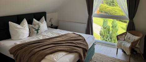 A bedroom with a bed, a chair, and a window with a view of greenery.