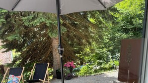 A patio area with wicker furniture, a glass table, and a large umbrella. - BergOase - Apart - am Feldberg mit Bergblick (Feldberg (Schwarzwald))