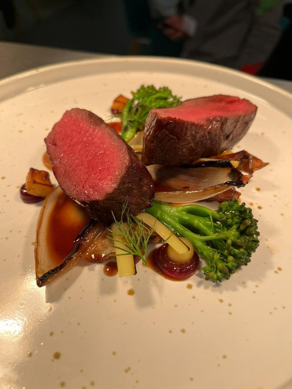 A plate of food with a slice of meat, vegetables, and sauce.