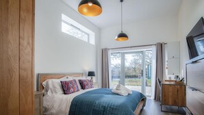 A bedroom with a bed, bedside table, lamp, and a view of the outdoors through a large window.