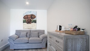 A living room with a grey sofa, a wooden cabinet with drawers, and a painting of an elephant on the wall. - Suite 10 - Sleeping Giant Hotel - Pen Y Cae Inn (Swansea Valley)