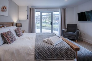 A modern hotel room with a large bed, a grey armchair, and a view of the outdoors through a sliding glass door. - Suite 7 - Sleeping Giant Hotel - Pen Y Cae Inn (Swansea Valley)