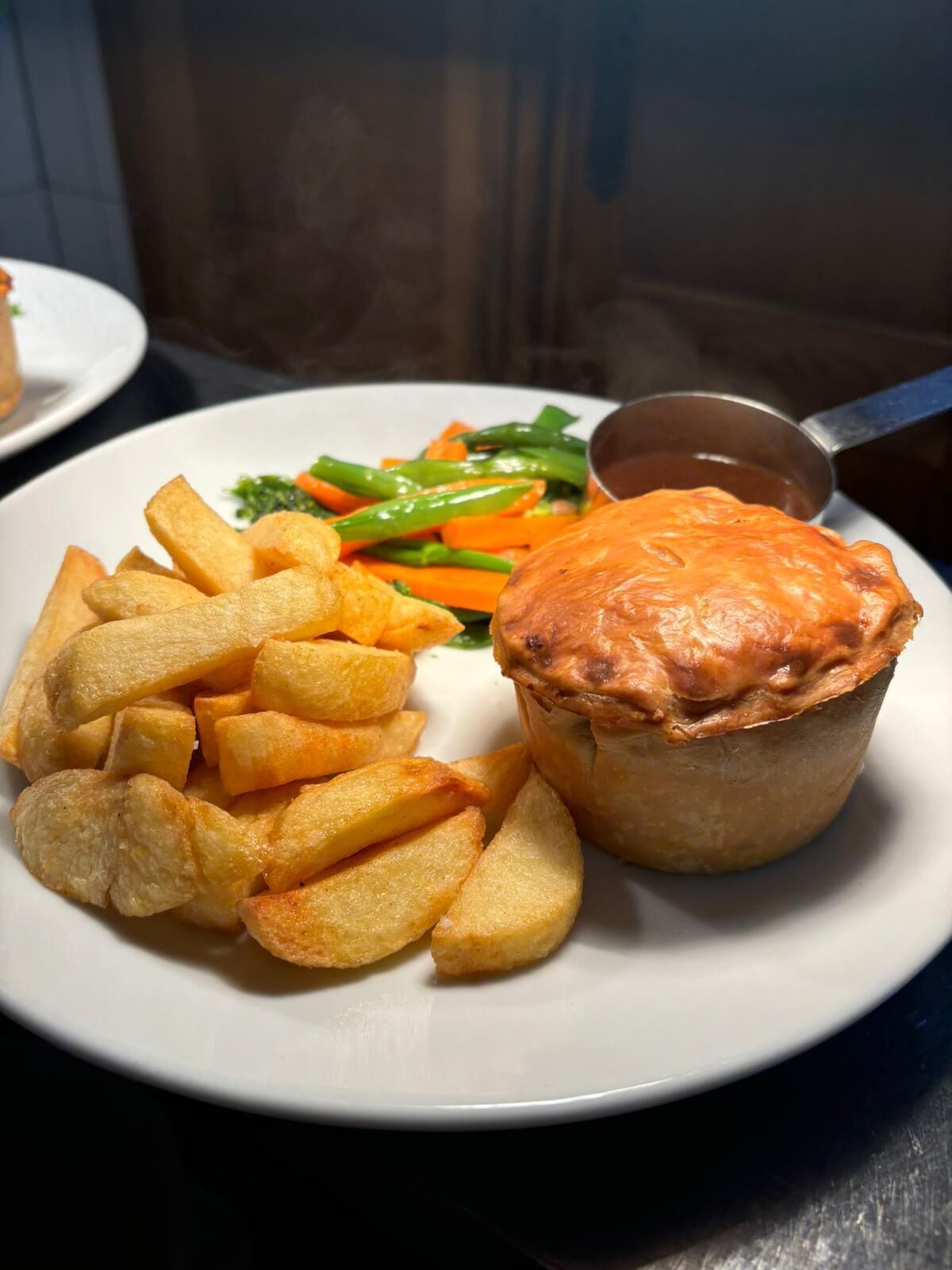 Une assiette contenant une tourte à la viande, des pommes de terre frites et des légumes cuits à la vapeur.