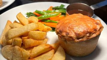 Une assiette contenant une tourte à la viande, des pommes de terre frites et des légumes cuits à la vapeur.