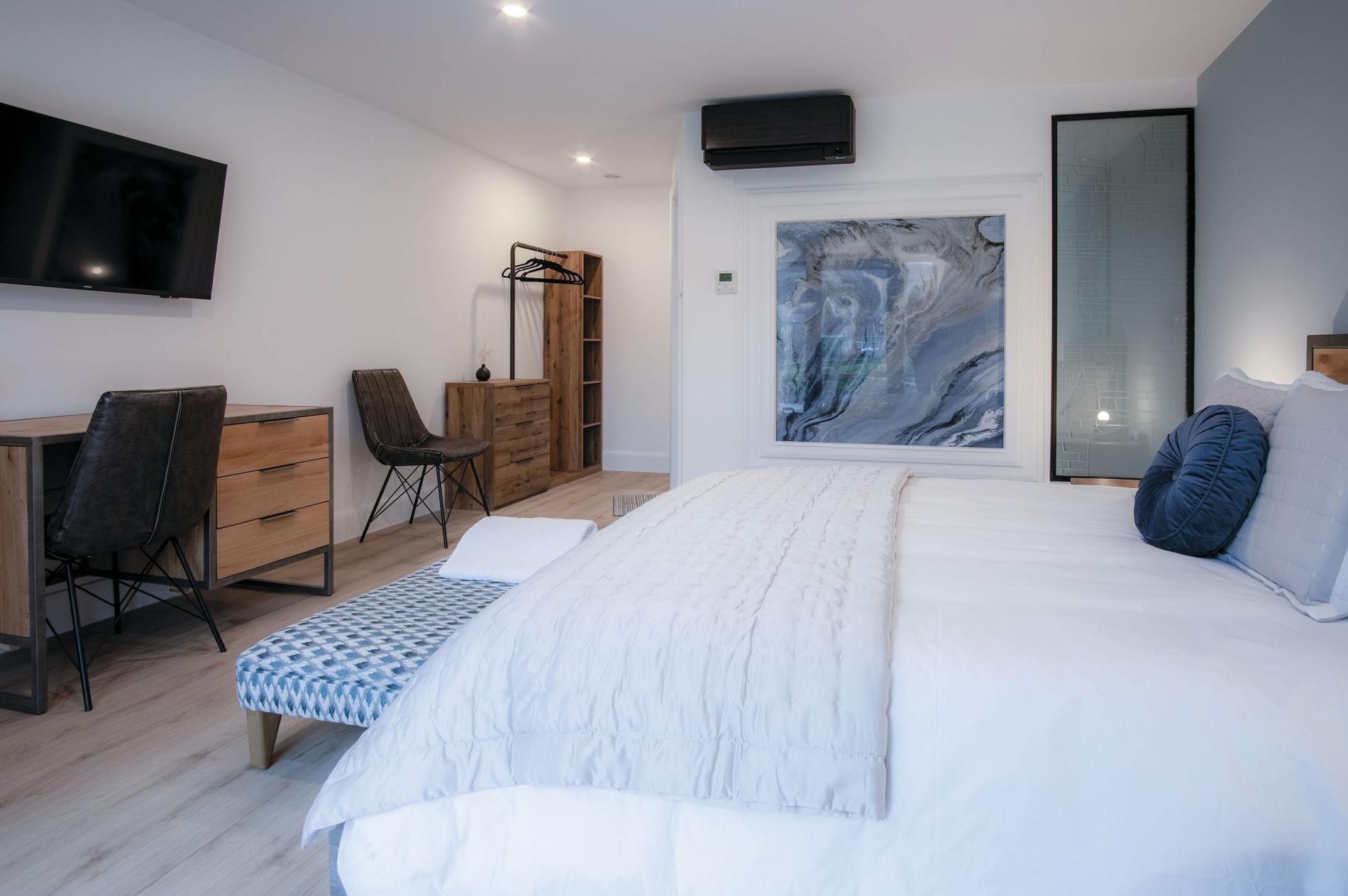 A modern bedroom with a large bed, a desk, a chair, and a wardrobe.
